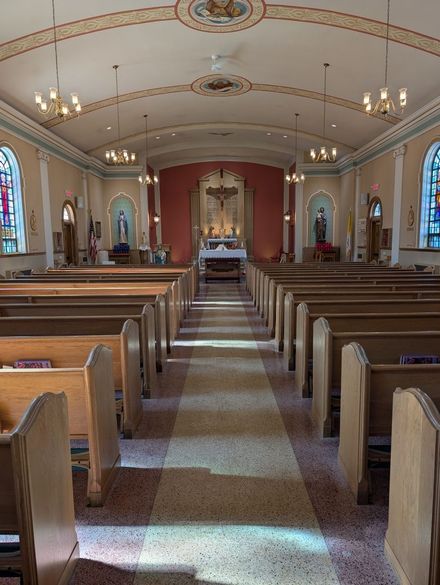 Interior of a small church with wooden pews, arched ceiling, and an altar at the far end