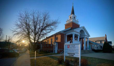 Brick church with white steeple at sunset, front sign, and bare trees on a quiet street.