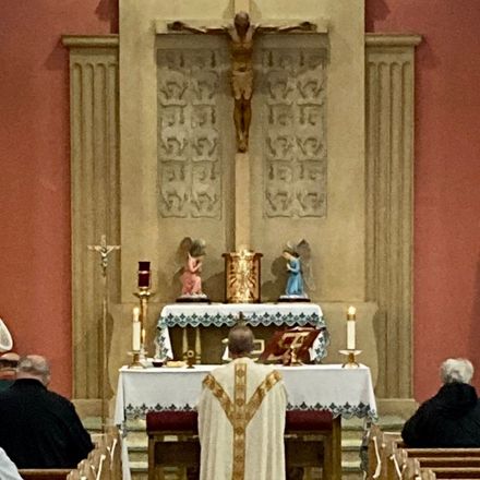 Catholic altar with crucifix, candles, statues, and priests seated during mass