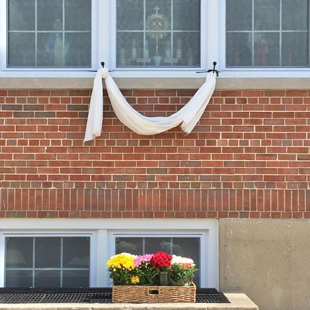 White cloth draped over a brick wall beneath windows, with a flower box on a lower ledge