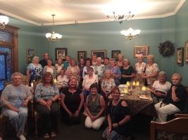 Large group posed in a teal living room around a glowing table centerpiece, with framed photos and chandeliers.