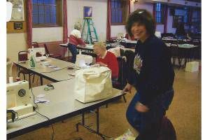 Person standing beside sewing machines in a classroom, smiling at the camera.
