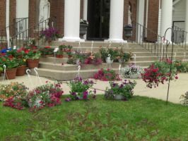 Front porch with white columns, brick house, and colorful potted flowers along the steps and lawn