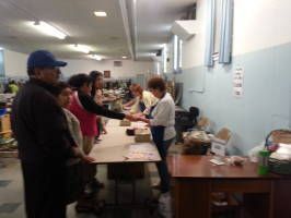People lined up at a table in a hallway, receiving items from a person behind it.