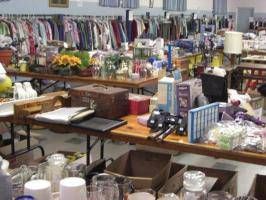 Tables covered with assorted household items and supplies in a cluttered indoor sale area.