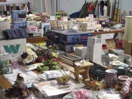 Cluttered table with books, cards, mugs, flowers, and small gift items in a room