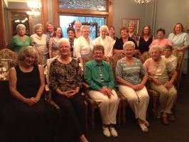 Group of smiling people posing indoors in a warmly lit room, seated and standing in two rows.