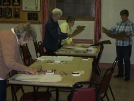 People sorting papers at tables in a community room during a meeting
