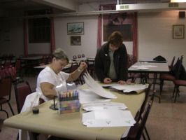 Two people working on papers at a table in a classroom or meeting room