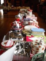 A long table lined with assorted wrapped gift baskets and containers in a dimly lit room.