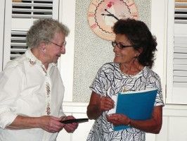 Two people smiling and talking indoors, one holding a blue folder and the other a tablet.