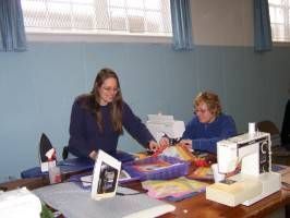 Two women at a table with papers and craft supplies in a blue-walled room