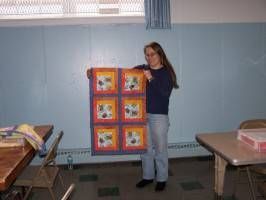 Person standing in a classroom holding an orange bulletin board with six colorful squares