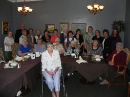 Group of people seated around tables in a dining room, posing for a group photo
