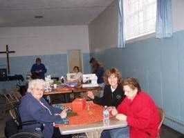 People seated at tables in a community hall, with a cross on the wall and large windows.