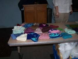 Table covered with colorful knitted items, with a person standing behind it in a room.