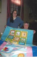 Woman standing behind an older person holding a colorful quilt indoors