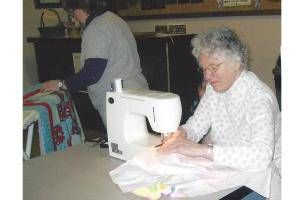 Woman sewing on a white machine beside folded fabric in a living room