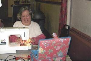 Woman sewing at a white machine beside a pink floral laptop in a cozy room
