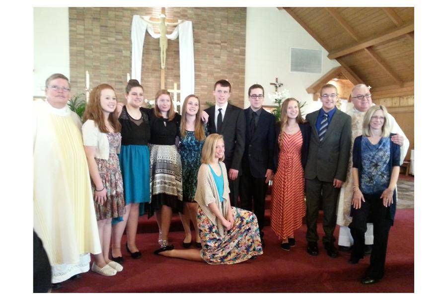 Group of people posing indoors in formal attire at a church or hall, with one woman seated in front