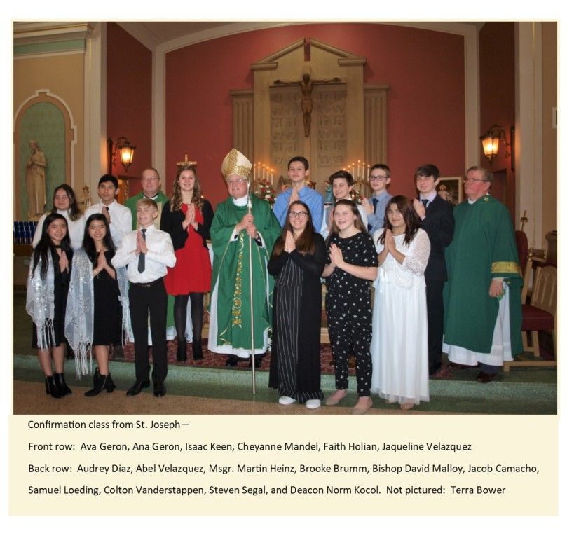 Confirmation class group posing in church before altar, with clergy in green vestments and teens in formal attire