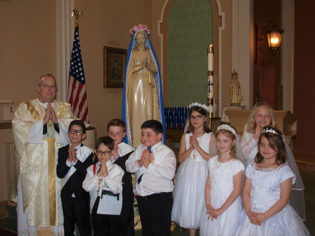 Priest and children posing in a church beside a statue of the Virgin Mary