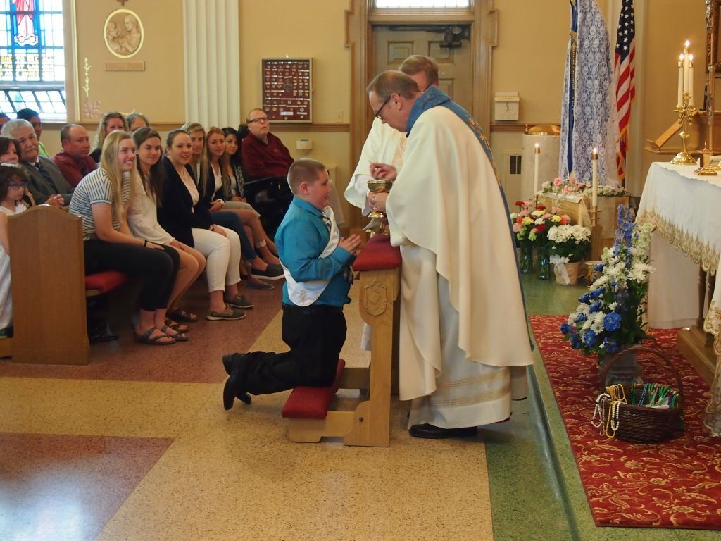 Man kneels to receive communion from a priest inside a church during a ceremony.