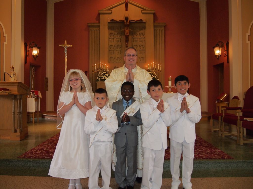 Children in white outfits posing with a priest in a church sanctuary