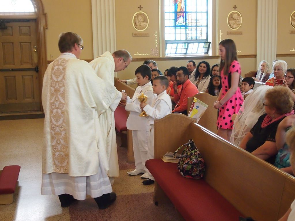 Children receiving communion from a priest inside a church, with seated congregation nearby.