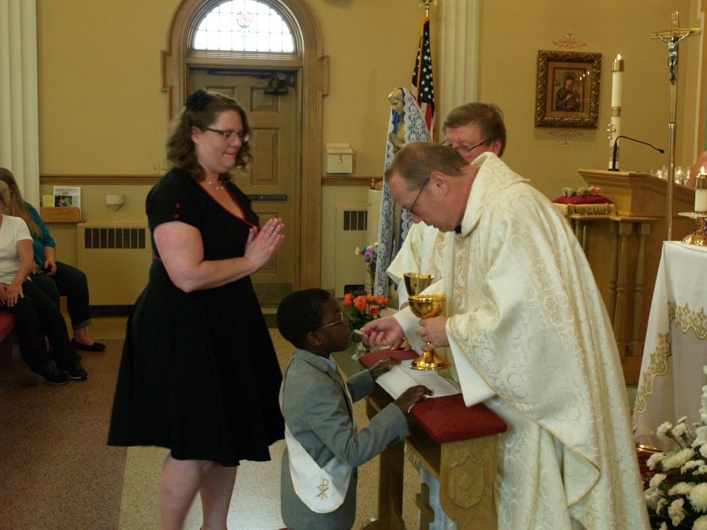 Priest giving communion to a child in a church, with a woman standing nearby