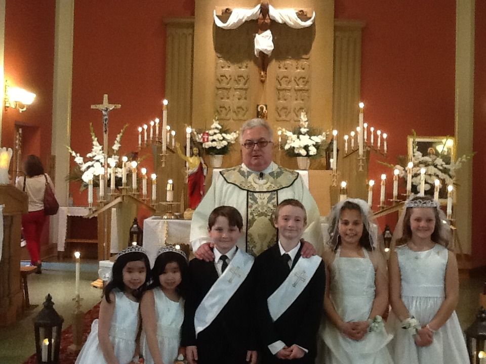 Children in formal attire stand with a priest in a church before the altar.
