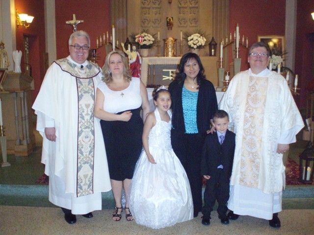 Wedding group posed in a church, with two priests, a bride, and two children in formal attire
