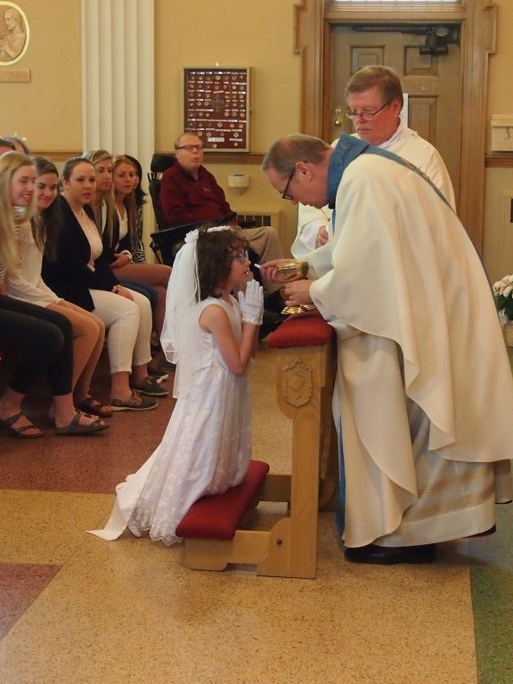 Girl kneels at church altar while a priest blesses her during communion ceremony