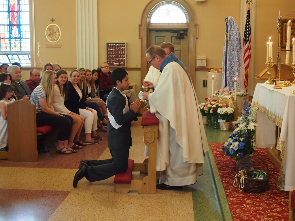 Person kneels before a priest at an altar during a church ceremony, with seated congregation nearby.