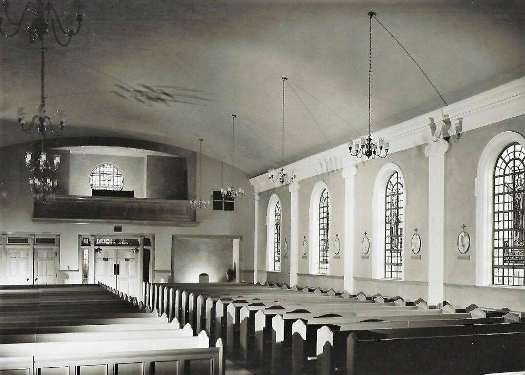 Empty church interior with pews, arched windows, and a balcony overlooking the nave