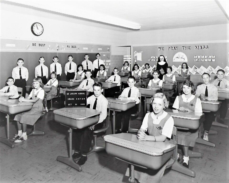 Classroom of students seated at desks, facing the camera in a black-and-white photo.