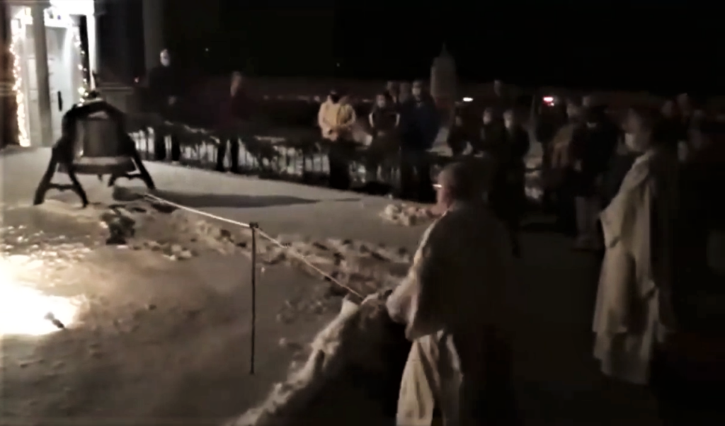 Nighttime outdoor scene with people gathered along a snowy path near a dark building.