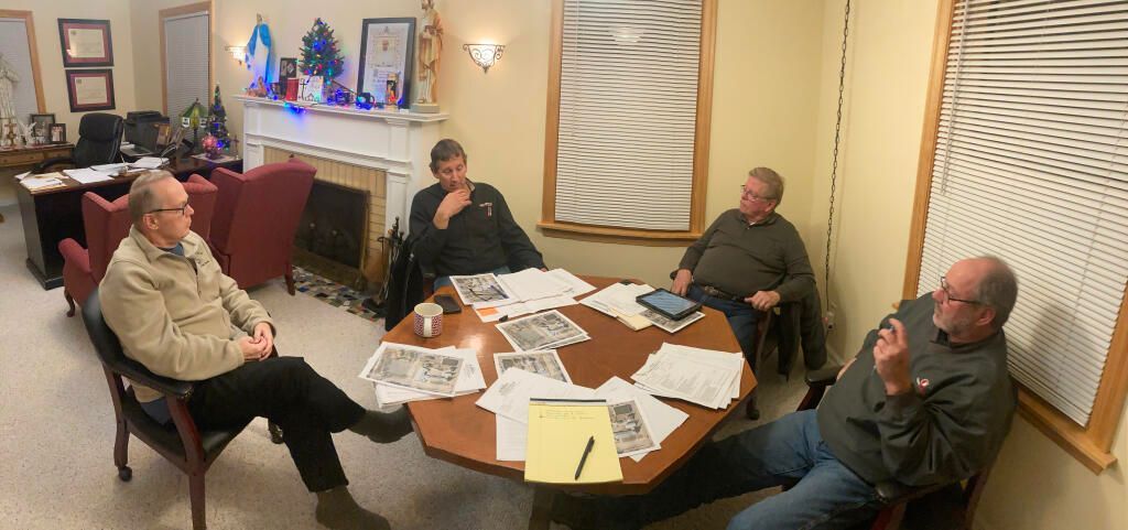 Five people sit around a table in a cozy room, surrounded by papers and decorations.