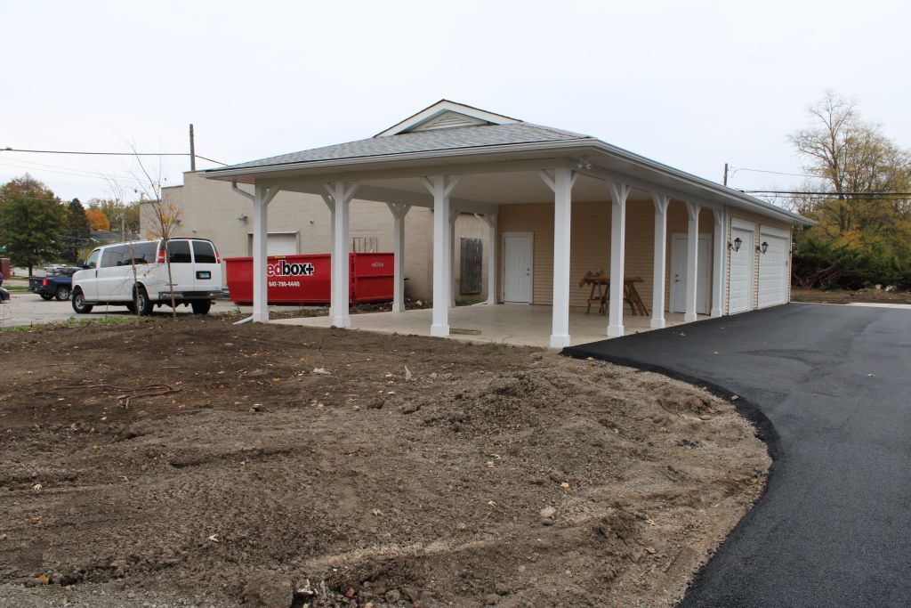 White pavilion-style building with columns beside a paved driveway and a parked white truck on an overcast day