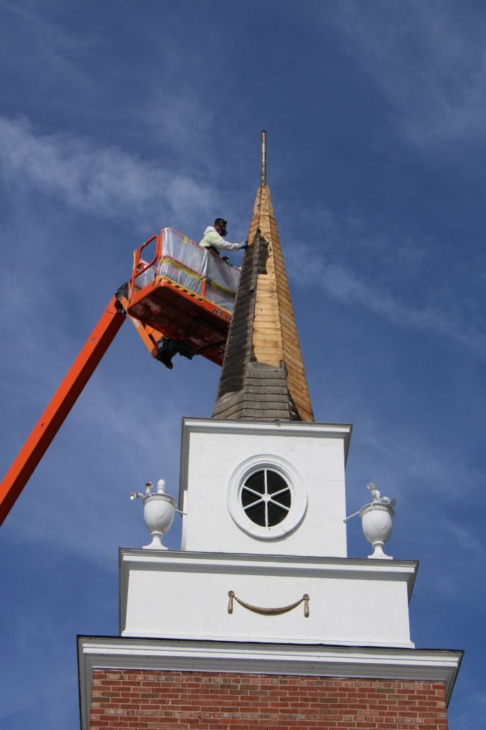Worker in an orange lift repairs a church steeple against a blue sky