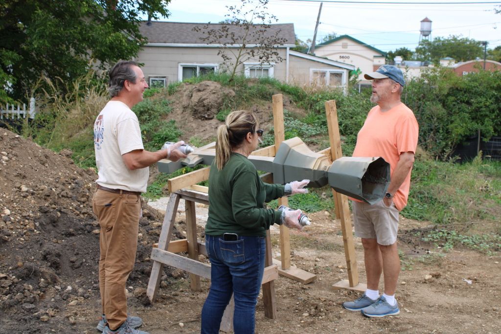 Three people work together pouring concrete into a wooden mold at an outdoor construction site.