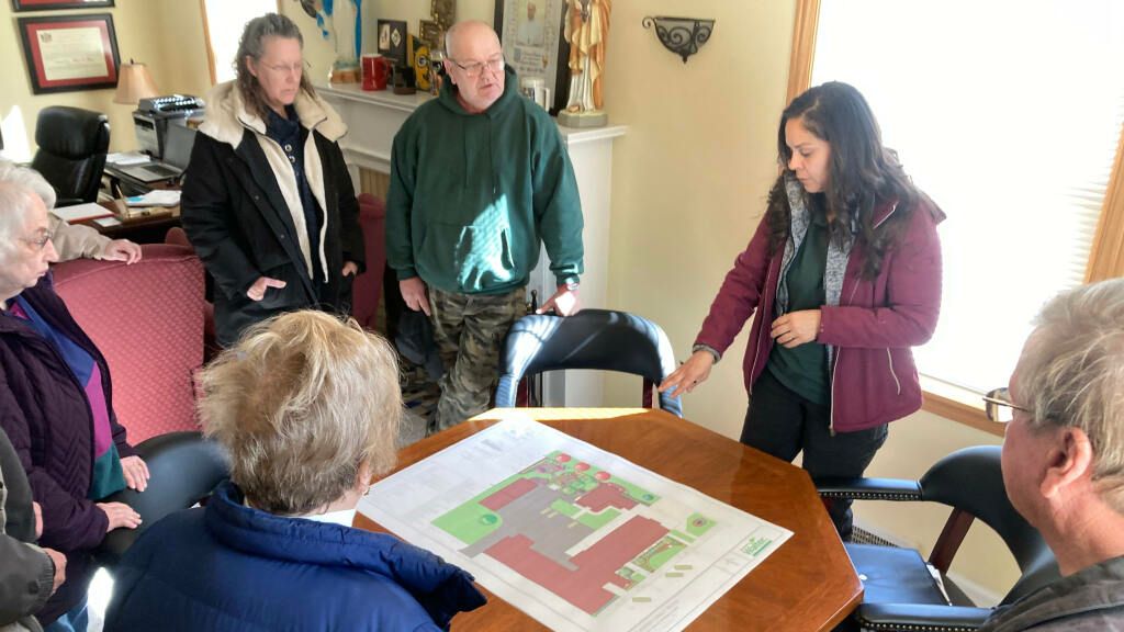 People gathered around a table reviewing a large printed floor plan in a bright room.