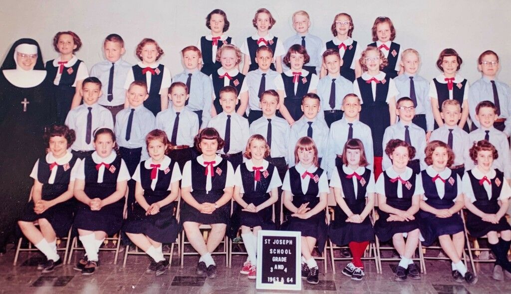 Group portrait of nuns and students in navy-and-white uniforms, seated and standing in rows indoors