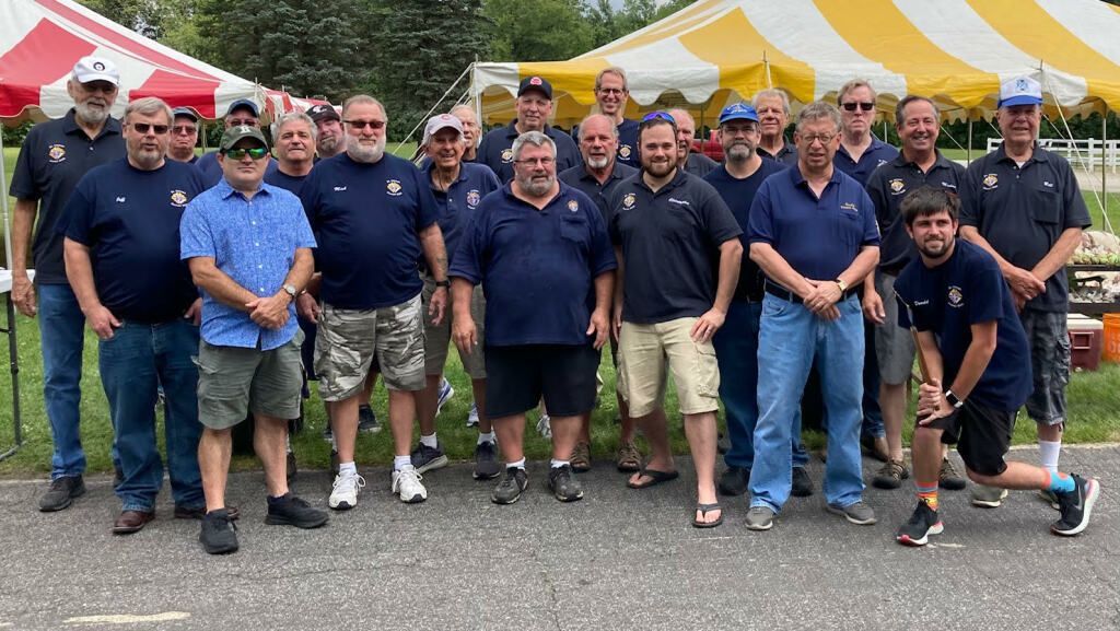 Group of people posing outdoors in front of red and yellow tents, many wearing navy shirts and caps.