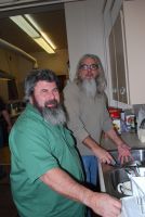 Two men in a kitchen, one in a green shirt washing dishes while the other stands nearby.