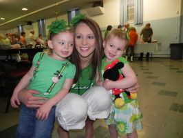 Woman kneeling with two children in a lobby, all smiling, one holding a stuffed toy.