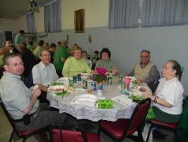 People seated around a banquet table in a community hall, chatting and eating.