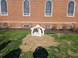 White nativity scene in front of a red brick building with arched windows, on a grassy lawn.
