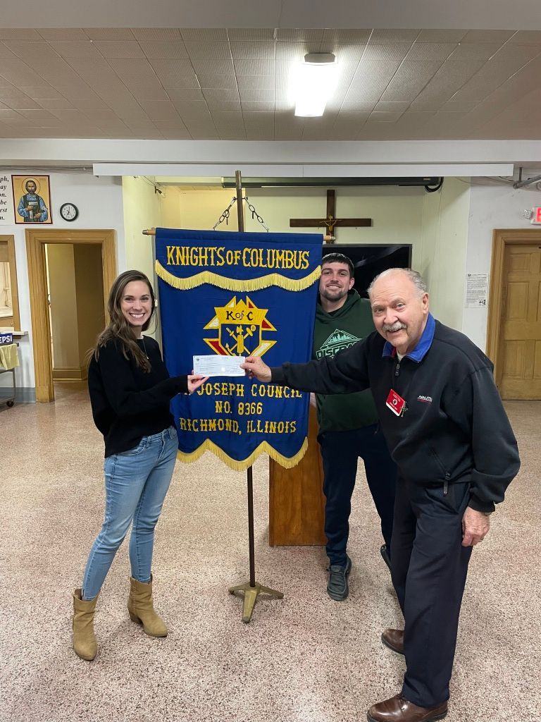 Three people pose with a blue Knights of Columbus banner in a hall.