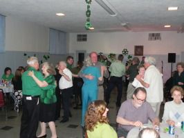 People dancing and socializing in a community hall with tables and chairs.